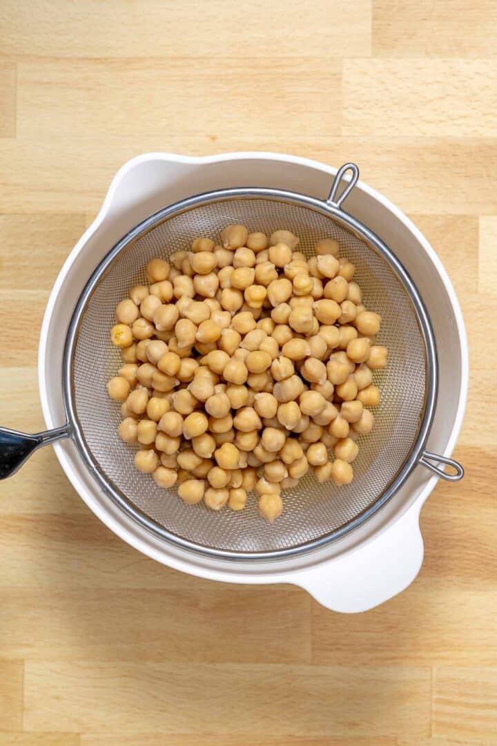 Draining chickpeas to use as the egg replacement in these vegan holiday cookies