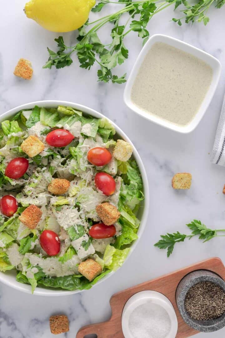 Gluten free Caesar Dressing in a square bowl on the side with, and on top of, a simple Caesar Salad